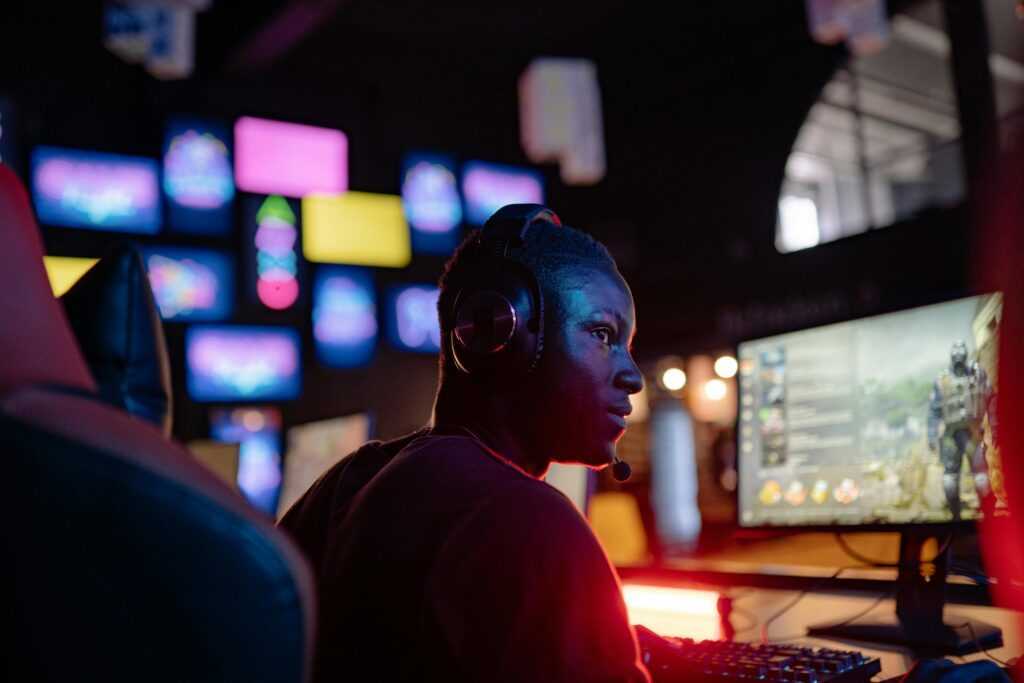 A young man intensely focused on a gaming session at a colorful gaming setup, wearing headphones.